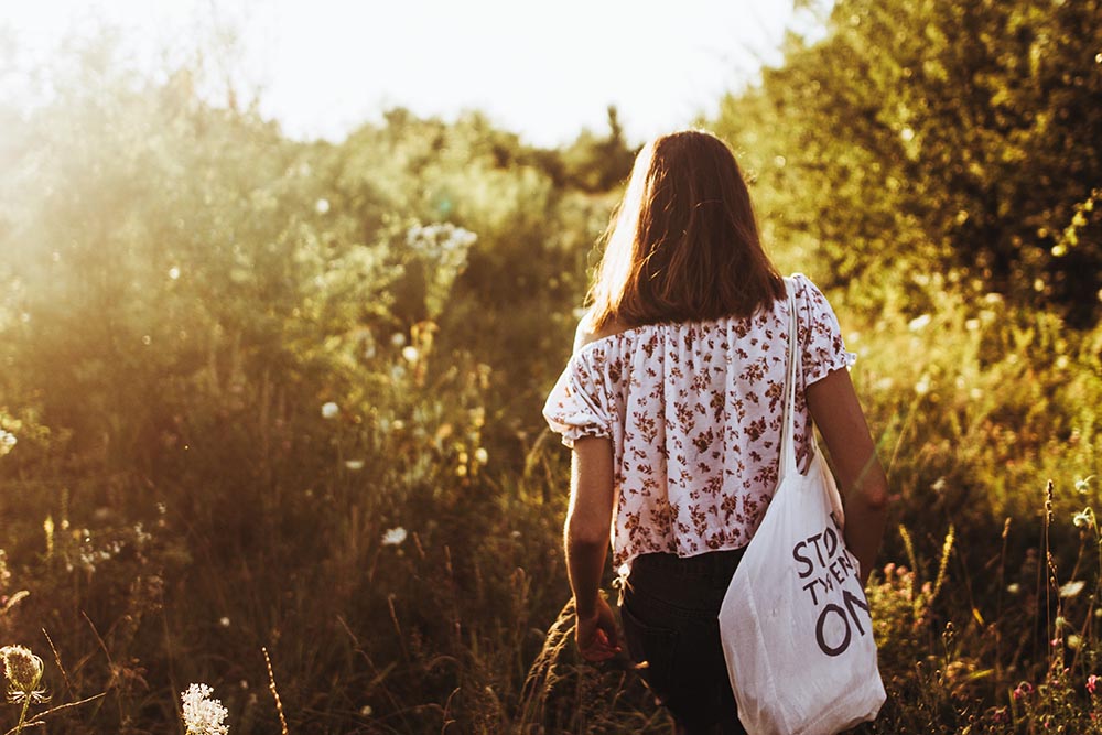 stylish hipster woman with eco bag walking into sunlight among w